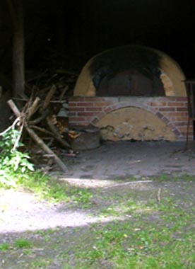 Bildmotiv zum Begriff "Backhaus" Verruster Lemofen auf Klinkerfundament mit Feuerholz im Garten vom Gut Karlshöhe