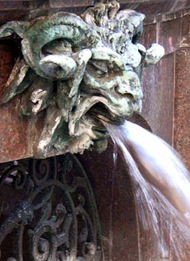 Wasserspeiender, grünlich patinierter Fratzenkopf am Hygieia-Brunnen